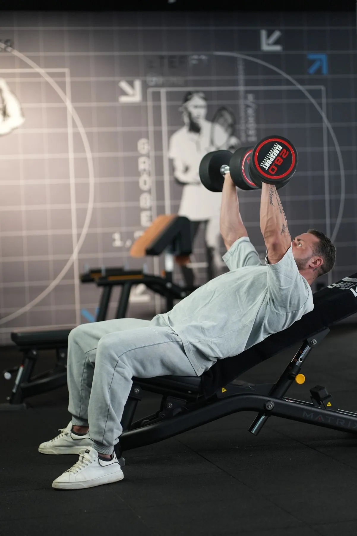 Der Coach trainiert mit zwei Kurzhanteln auf einer Schrägbank im Fitnessstudio.